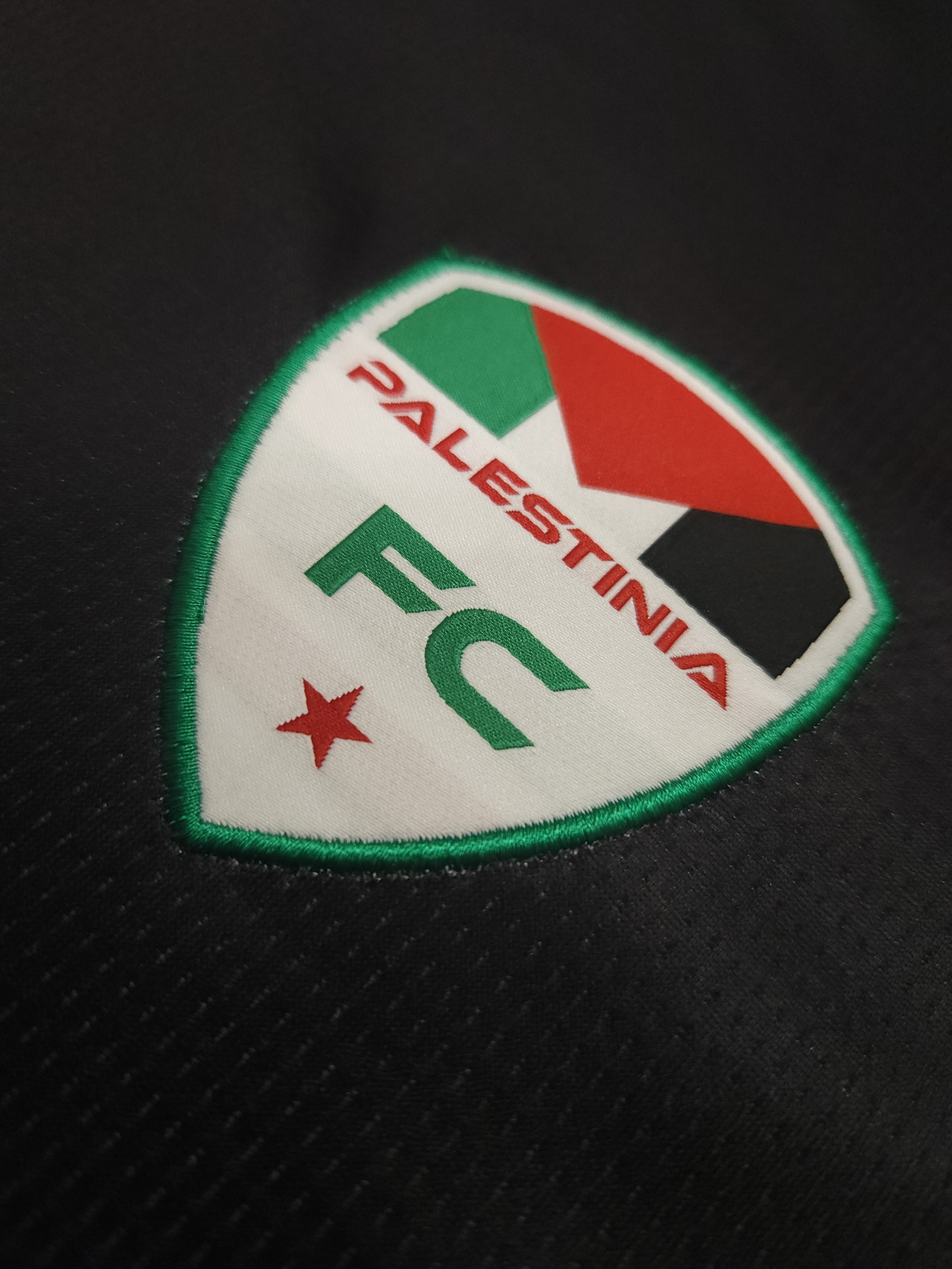 Close-up of Palestinia FC embroidered crest with Palestinian flag colors on black football jersey
