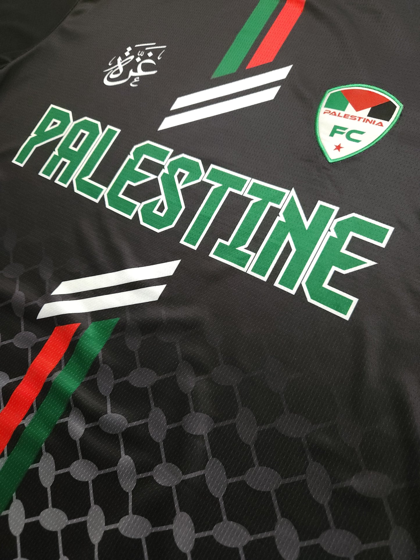 Close-up of Black Palestine football jersey showing Palestinia FC crest, red and green stripes, and keffiyeh-pattern fabric
