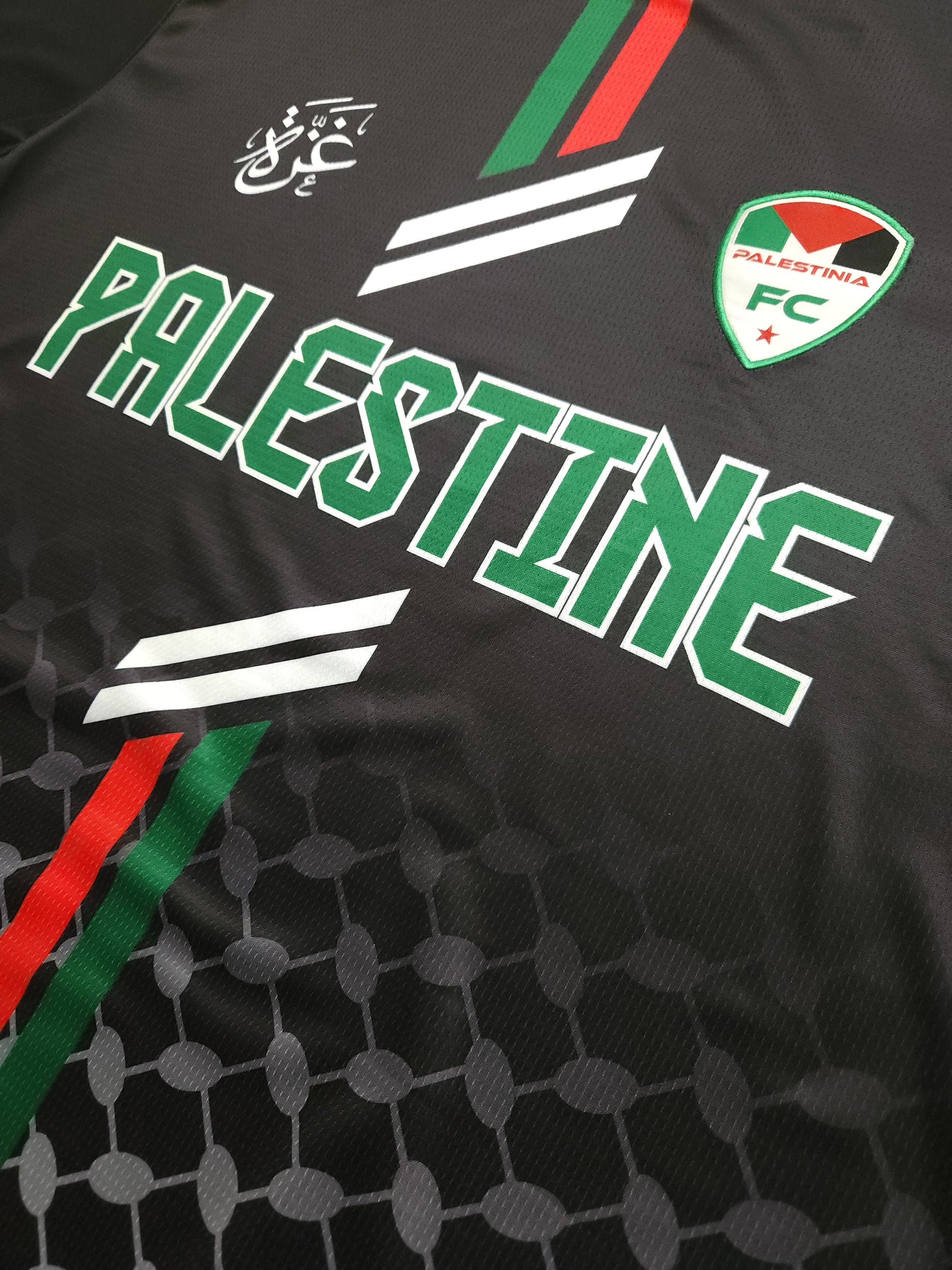 Close-up of Black Palestine football jersey showing Palestinia FC crest, red and green stripes, and keffiyeh-pattern fabric