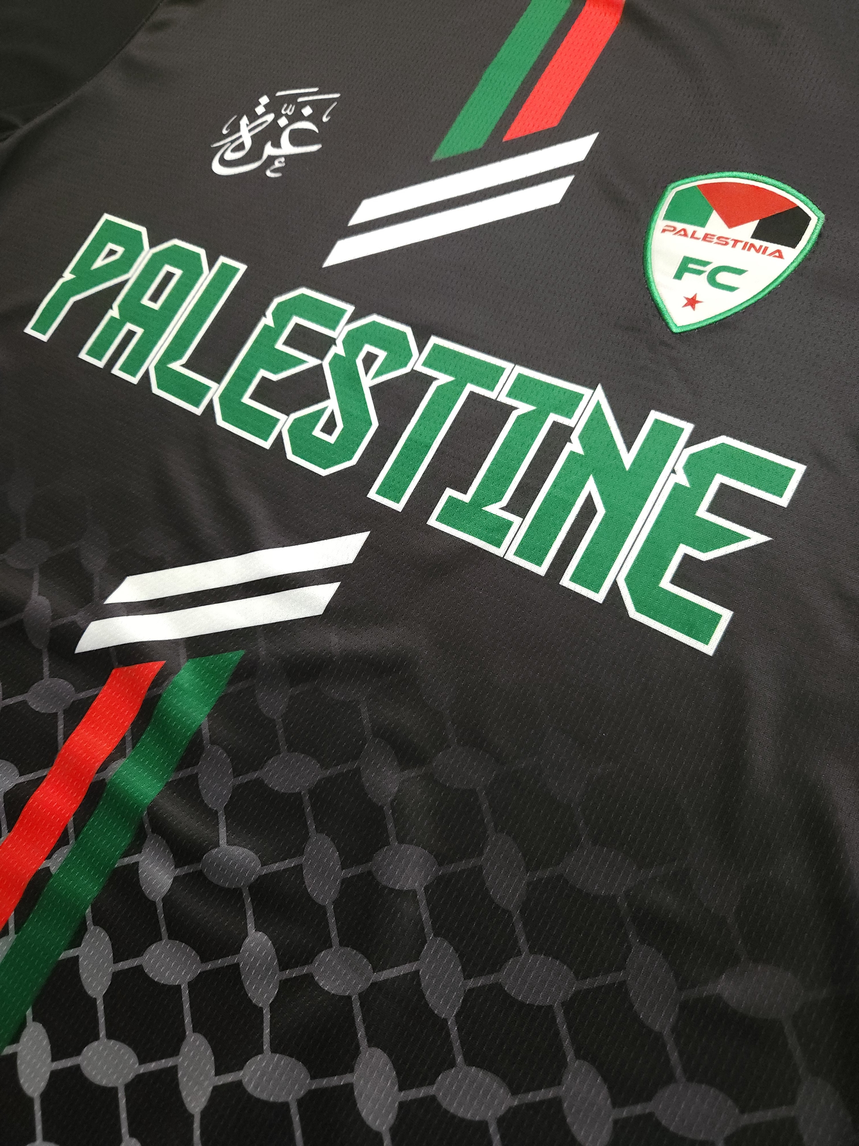 Close-up of Black Palestine football jersey showing Palestinia FC crest, red and green stripes, and keffiyeh-pattern fabric