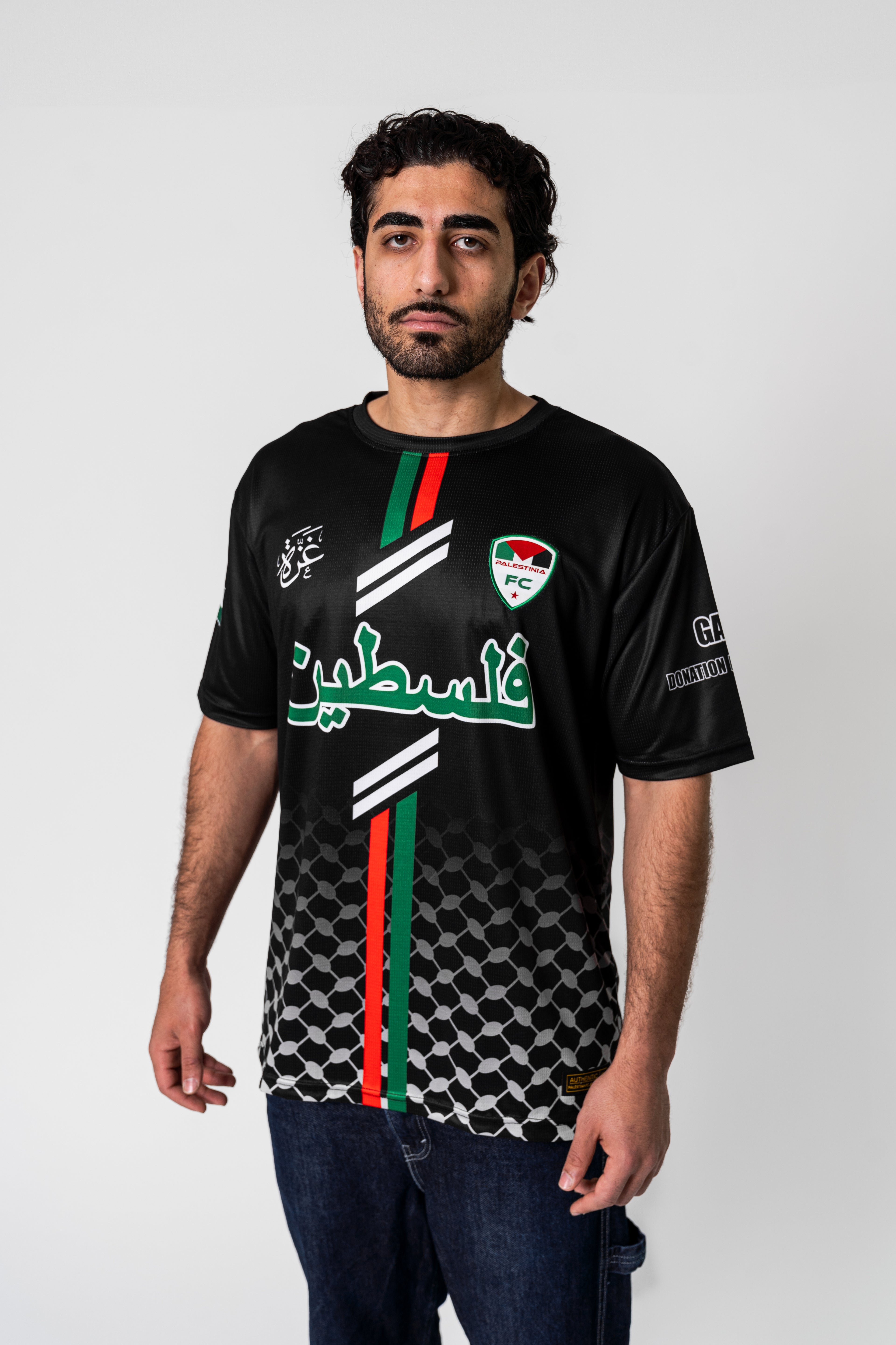 Model wearing black Palestinia FC Arabic jersey featuring keffiyeh pattern, red and green flag stripes, and embroidered crest