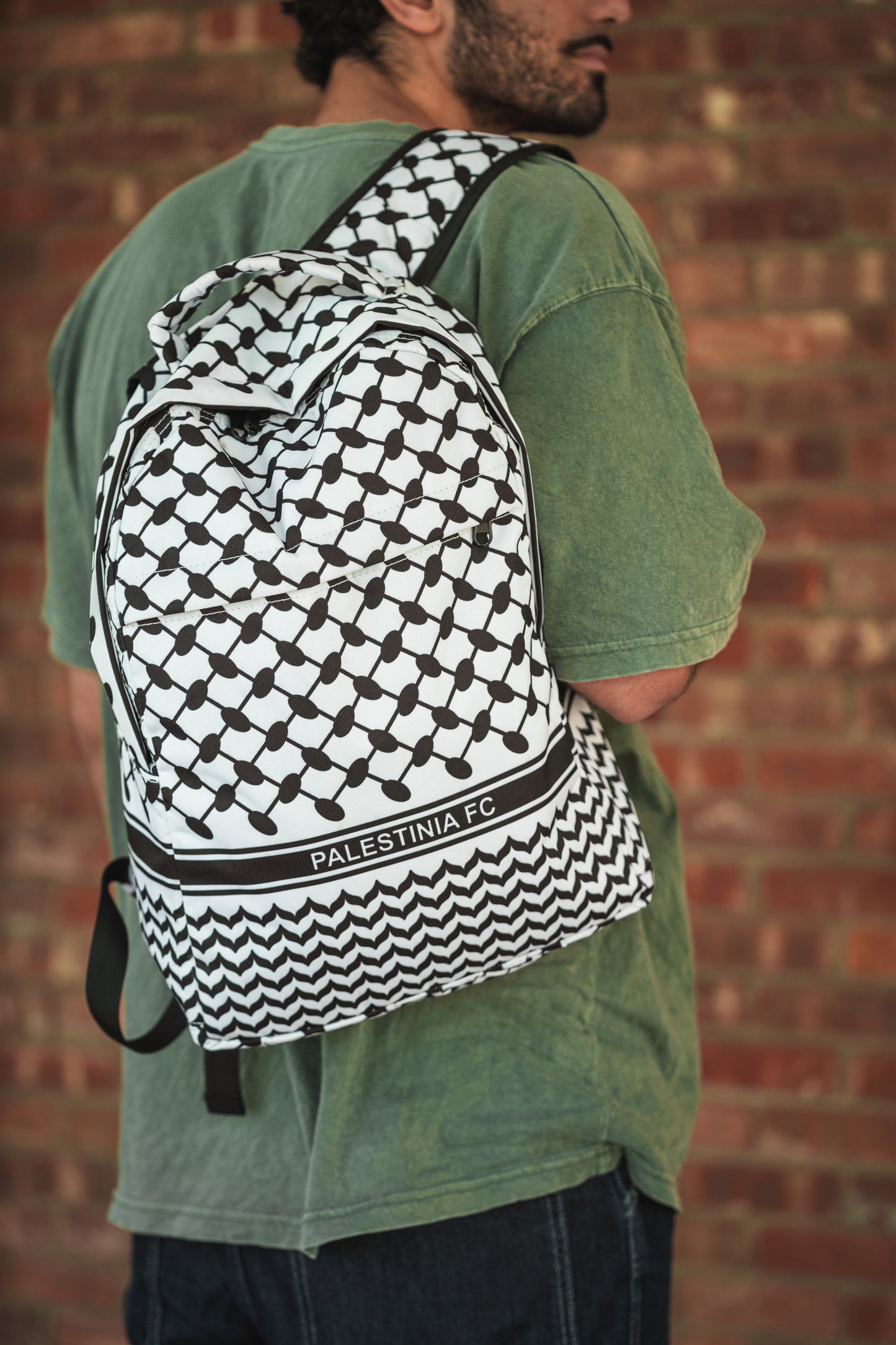Person wearing Palestinia FC Keffiyeh Backpack with kufiya pattern and Palestinia FC branding against brick wall background