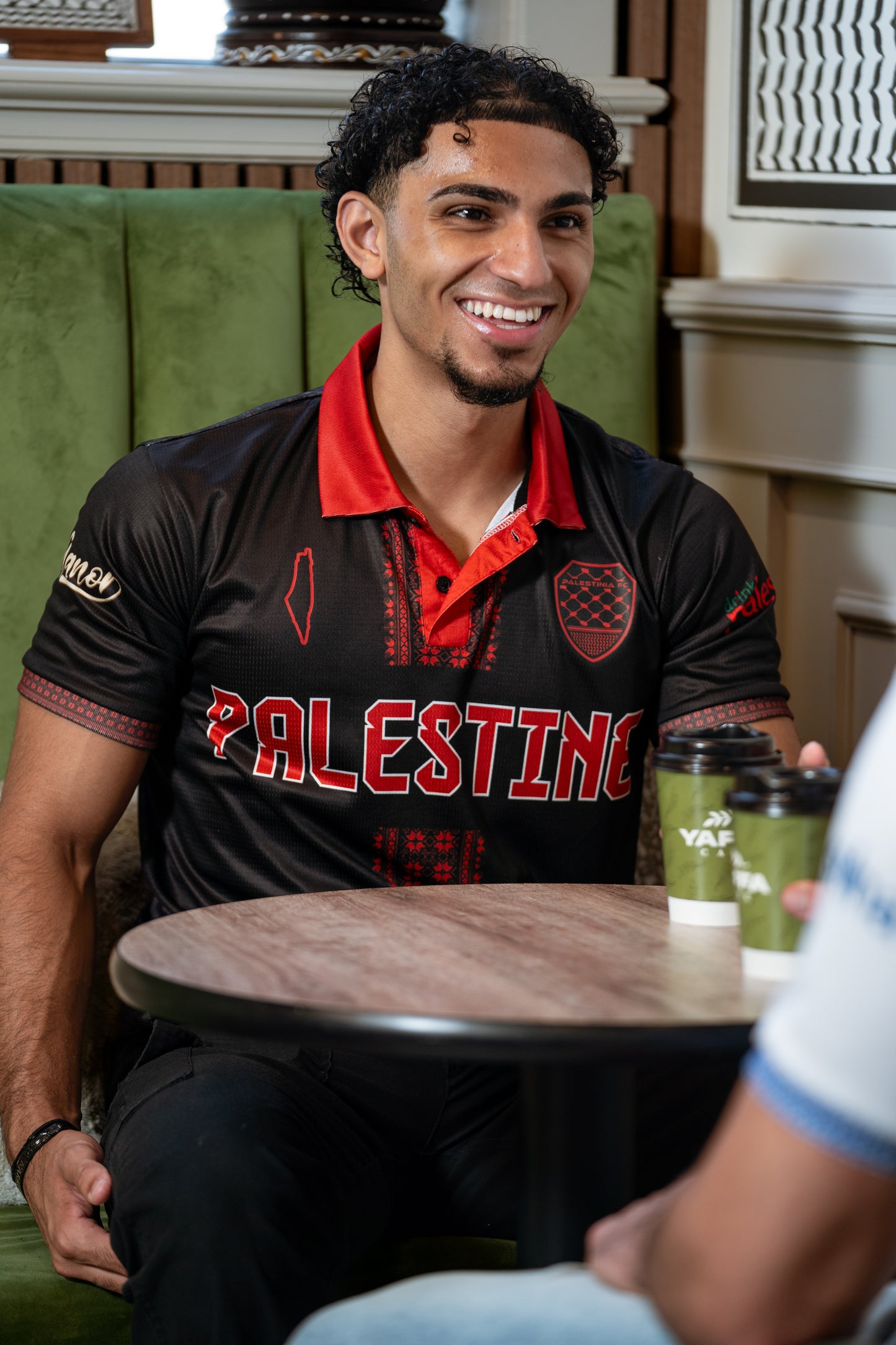 Person wearing a black and red shirt with 'PALESTINE' printed on it, sitting at a table.