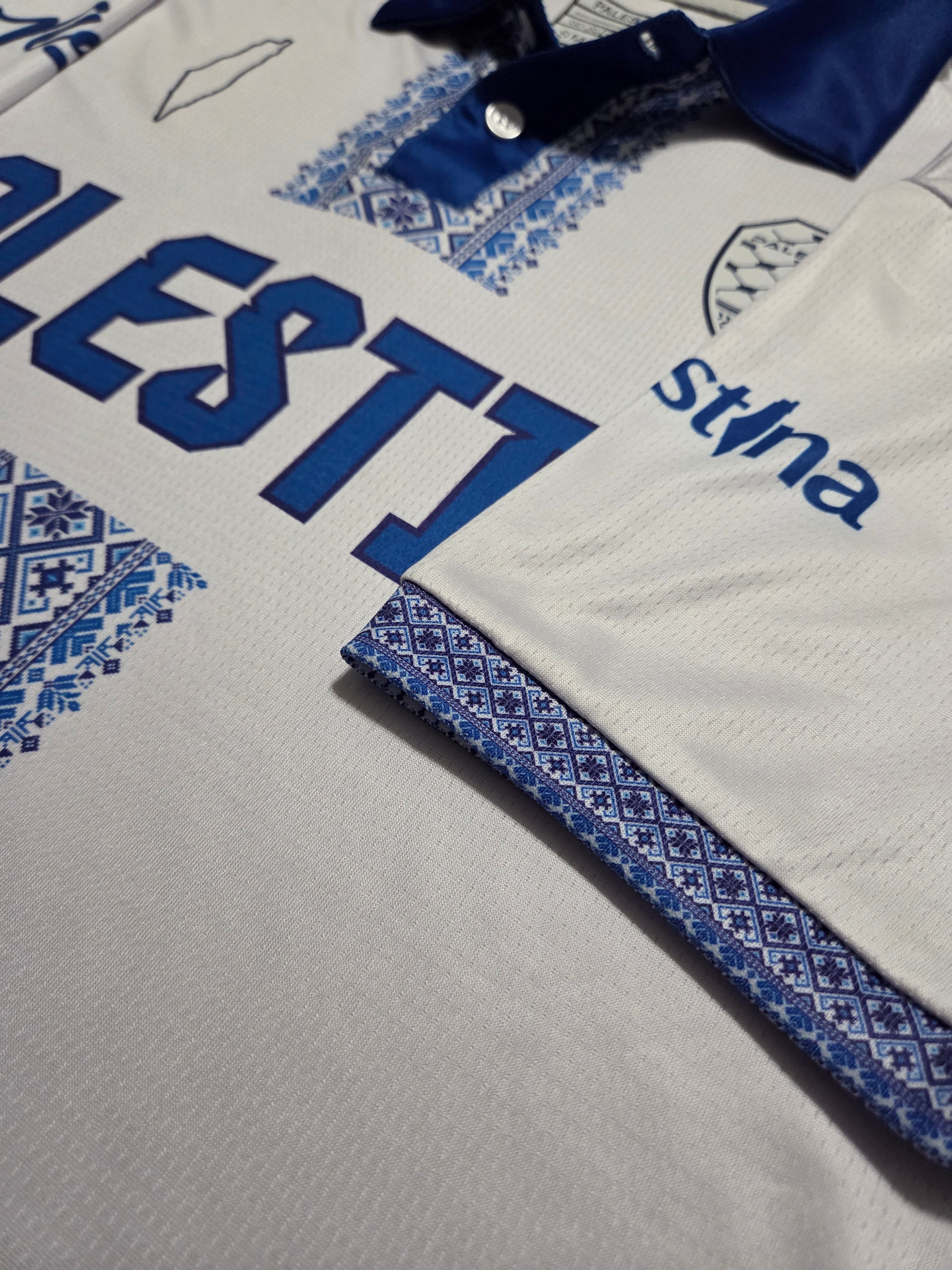 Close-up of blue Tatreez embroidery and Palestine logo on white jersey