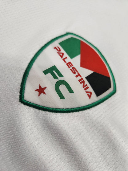 Close-up of Palestinia FC embroidered crest on white football jersey featuring Palestinian flag colors