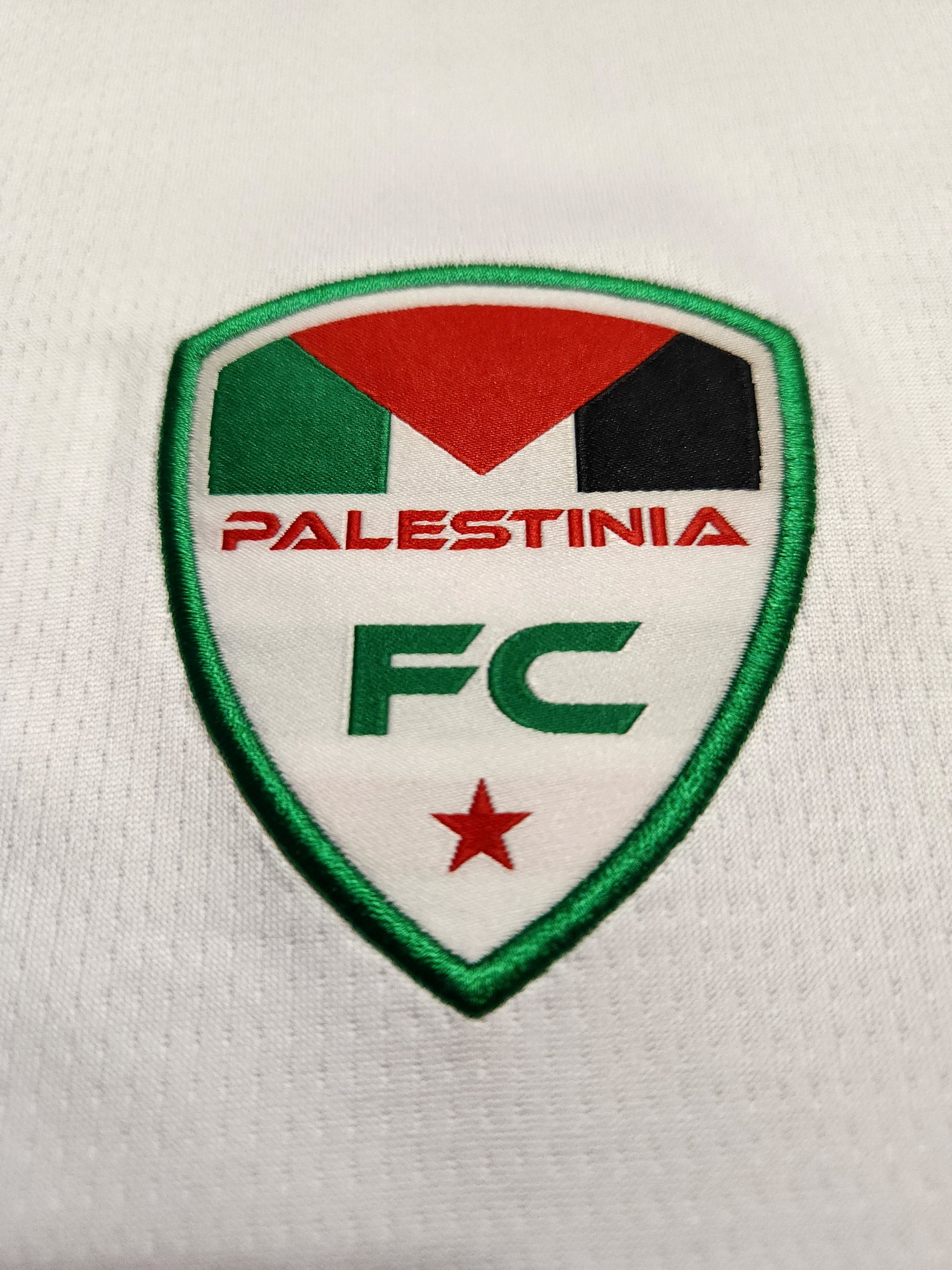 Close-up of embroidered Palestinia FC crest on white Arabic jersey with red, green, and black flag design and star emblem
