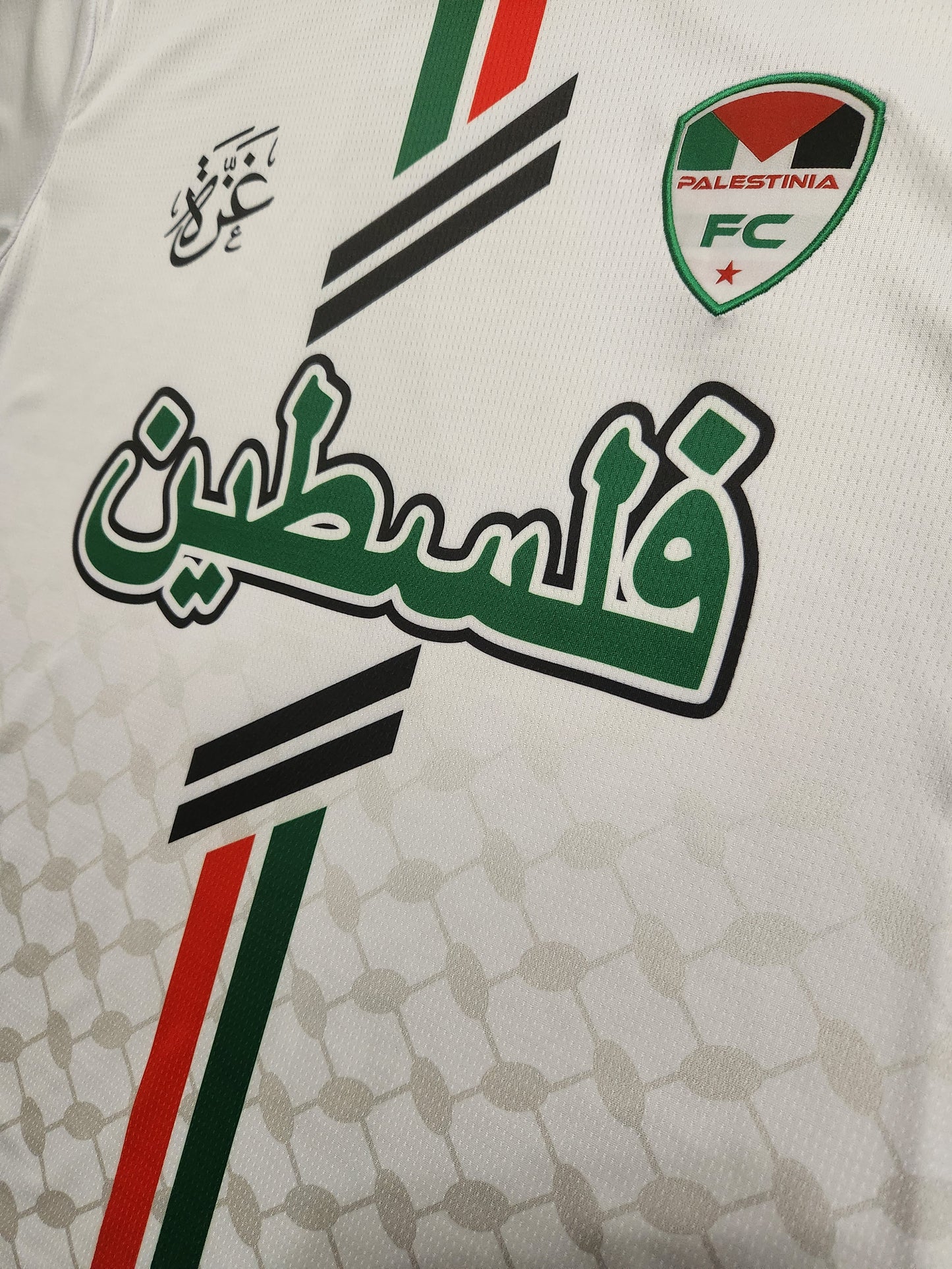 Close-up of Arabic text and Palestinia FC crest on white jersey with keffiyeh pattern